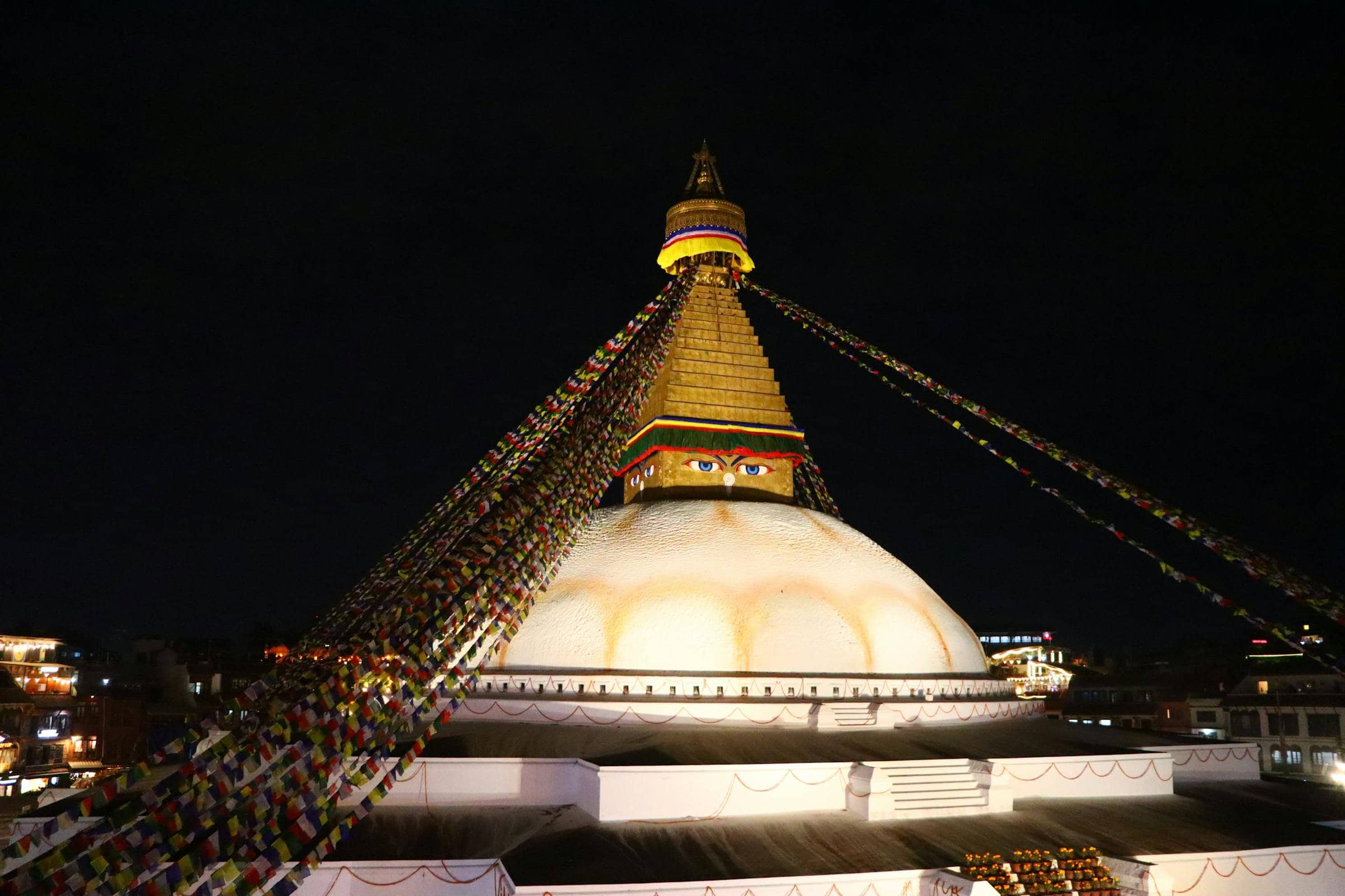 Boudhanath stupa illuminated at dusk, prayer flags streaming overhead — Kathmandu, Nepal.